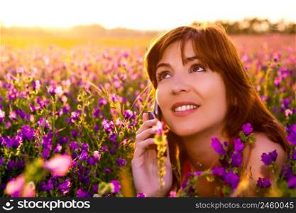 Beautiful young woman lying on the nature and talking at cellphone