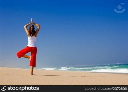 Beautiful young woman making Yoga exercises on the beach