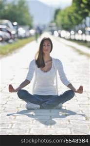 beautiful young woman meditating and exercise yoga in lotus position at street at beautiful sunny day with blured background