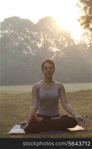 Beautiful young woman meditating in park