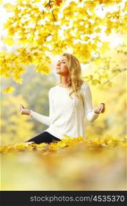 Beautiful young woman meditating outdoors in autumn park