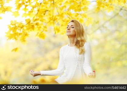 Beautiful young woman meditating outdoors in autumn park