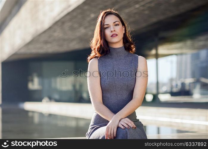 Beautiful young woman, model of fashion, sitting in urban background