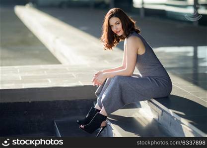 Beautiful young woman, model of fashion, sitting in urban background. Girl smiling.