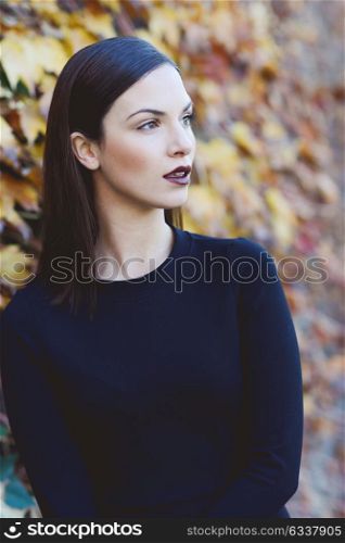 Beautiful young woman, model of fashion, wearing black dress in urban background with autumn colors. Very straight hair styling