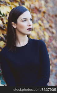 Beautiful young woman, model of fashion, wearing black dress in urban background with autumn colors. Very straight hair styling