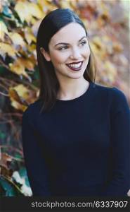 Beautiful young woman, model of fashion, wearing black dress smiling in urban background with autumn colors. Very straight hair styling