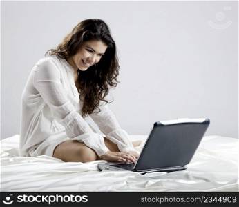 Beautiful young woman on bed working with a laptop