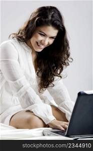 Beautiful young woman on bed working with a laptop