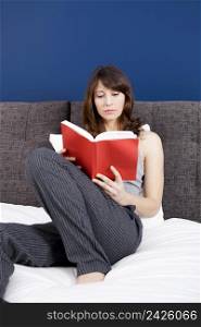 Beautiful young woman on the bed reading a book