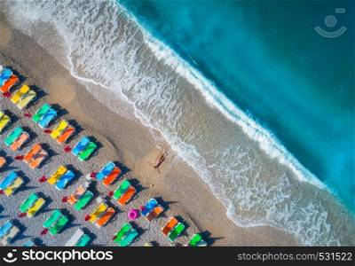 Beautiful young woman on the sea at sunrise in Oludeniz, Turkey. Aerial view of lying woman on the beach with colorful chaise-lounges. Top view from drone. Seascape with girl, azure water and waves. Aerial view of lying woman on the beach