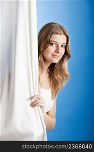 Beautiful young woman peeking behind a white sheet