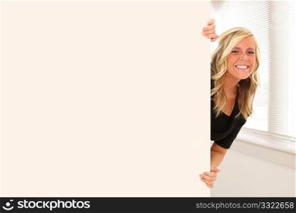 Beautiful young woman peeking out behind wall of office or school building.