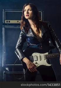 Beautiful young woman playing electruc guitar on stage in front of large amplifier.