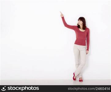 Beautiful young woman pointing to the right side with copyspace, against a white wall