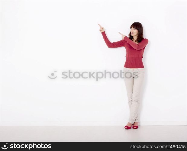 Beautiful young woman pointing to the right side with copyspace, against a white wall