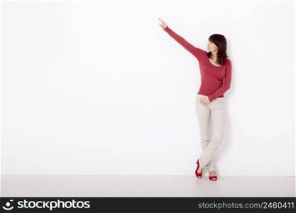 Beautiful young woman pointing to the right side with copyspace, against to a white wall