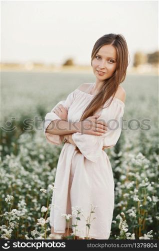 Beautiful young woman portrait in field. Attractive brunette girl with long curly hair style in white dress dreaming. portrait of beautiful long-haired girl.. Beautiful young woman portrait in field. Attractive brunette girl with long curly hair style in white dress dreaming. portrait of beautiful long-haired girl