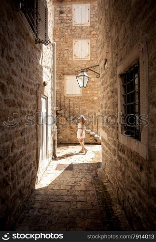 Beautiful young woman posing on old narrow street at sunny day
