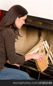 Beautiful young woman putting wood logs into home fireplace