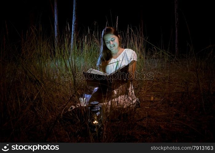 Beautiful young woman reading magic book at dark night forest