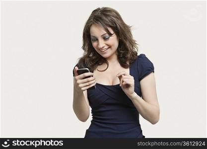 Beautiful young woman reading text message on cell phone over gray background