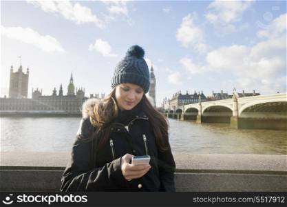 Beautiful young woman reading text message through smart phone by river Thames; London; UK