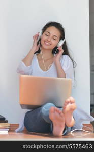 beautiful young woman relax and work on laptop computer while listening music on heaphones and read book at home