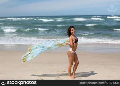Beautiful young woman relaxing at the beach and holding a white fabric