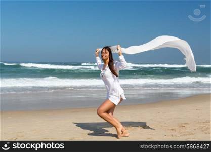 Beautiful young woman relaxing at the beach and holding a white fabric
