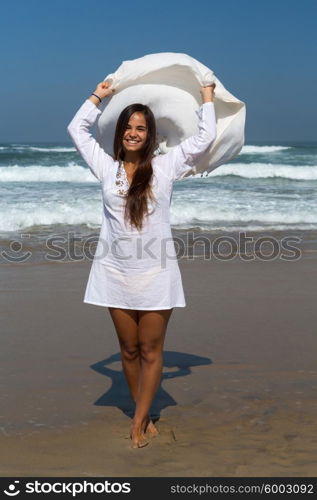 Beautiful young woman relaxing at the beach and holding a white fabric