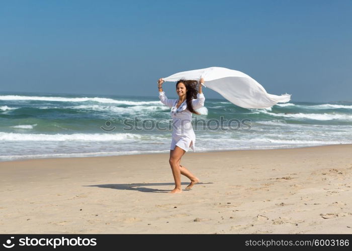 Beautiful young woman relaxing at the beach and holding a white fabric