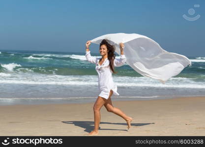 Beautiful young woman relaxing at the beach and holding a white fabric