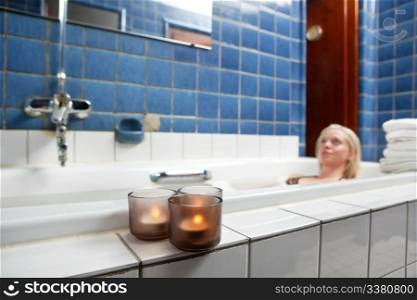 Beautiful young woman relaxing in bathtub with candles in foreground
