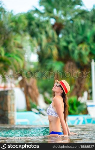 Beautiful young woman relaxing in swimming pool in outdoor pool. Beautiful young woman relaxing in swimming pool. Girl in red bikini in outdoor pool at luxury hotel