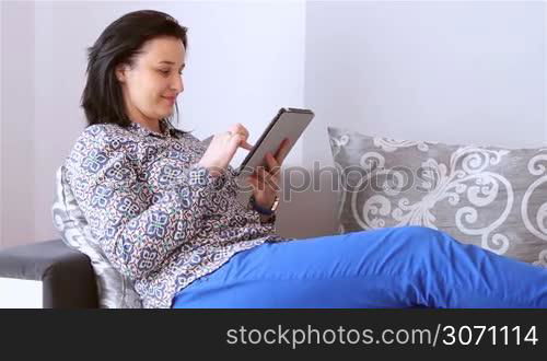 Beautiful young woman relaxing with a digital tablet computer in her living room.
