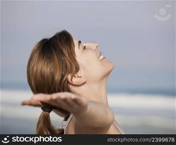 Beautiful young woman relaxing with arms open on the beach