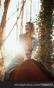 Beautiful young woman riding her brown horse and wearing dress