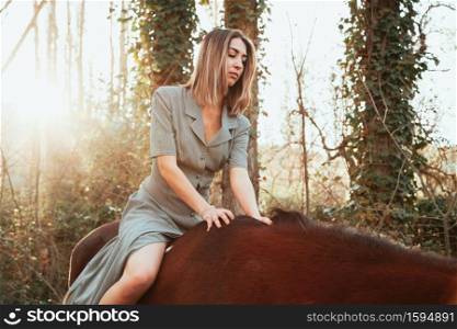 Beautiful young woman riding her brown horse and wearing dress
