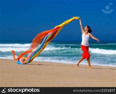 Beautiful young woman running on the beach with a colored tissue