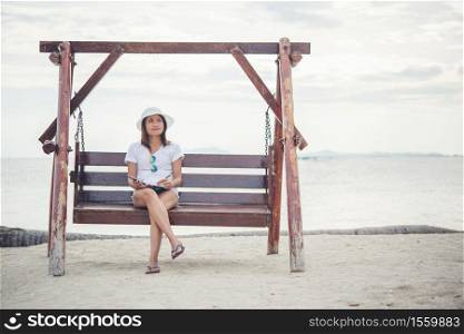Beautiful young woman sat on a swing between writing on her notepad. woman Relaxing near on the beach.