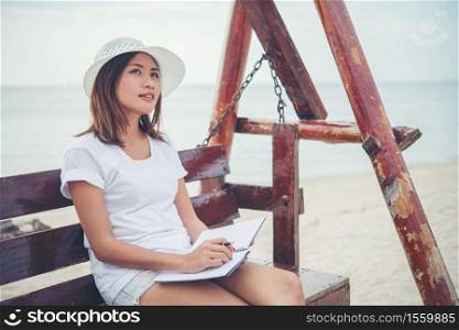 Beautiful young woman sat on a swing between writing on her notepad. woman Relaxing near on the beach.
