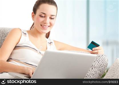 Beautiful Young Woman Shopping Online on Laptop with a Credit Card, Sitting on the Sofa in Living Room