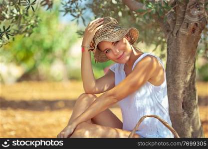 Beautiful young woman sitting and resting under the tree in the garden, enjoying nice warm spring day, spending leisure time outdoors, happy spring holidays