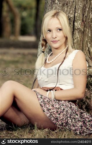 Beautiful young woman sitting close to a tree and thinking on something