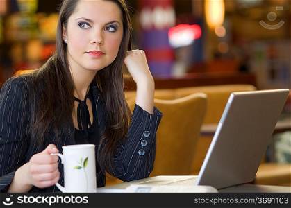 beautiful young woman sitting in a bar with laptop and a cup of tea