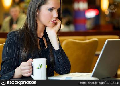 beautiful young woman sitting in a bar with laptop and cup of tea