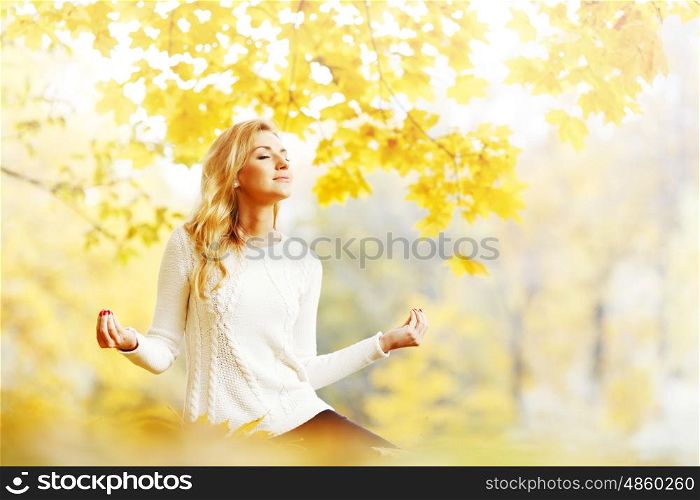 Beautiful young woman sitting in autumn park in lotus yoga position. Yoga woman in autumn park
