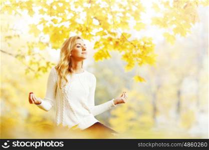 Beautiful young woman sitting in autumn park in lotus yoga position. Yoga woman in autumn park