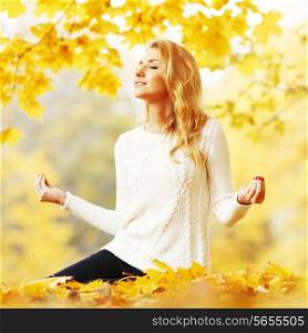 Beautiful young woman sitting in autumn park in lotus yoga position
